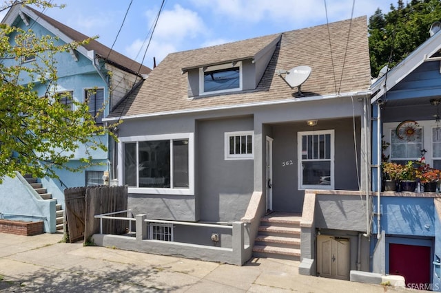 bungalow-style home with roof with shingles, fence, and stucco siding