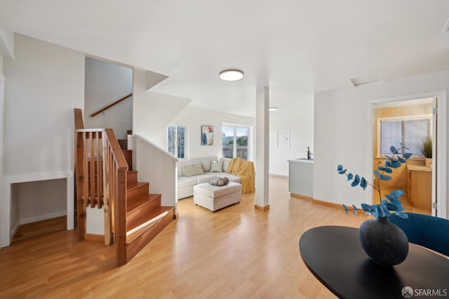 living area featuring light wood-style flooring, baseboards, and stairs