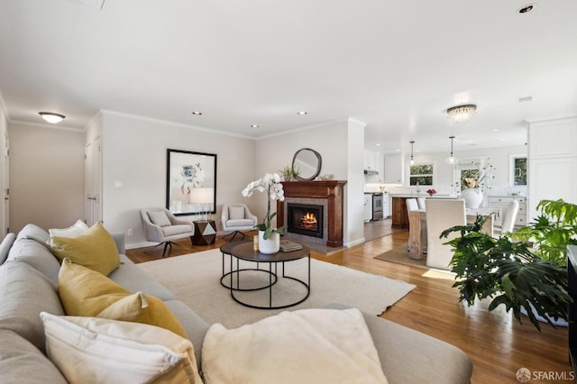 living room featuring baseboards, light wood-style flooring, recessed lighting, a fireplace, and crown molding