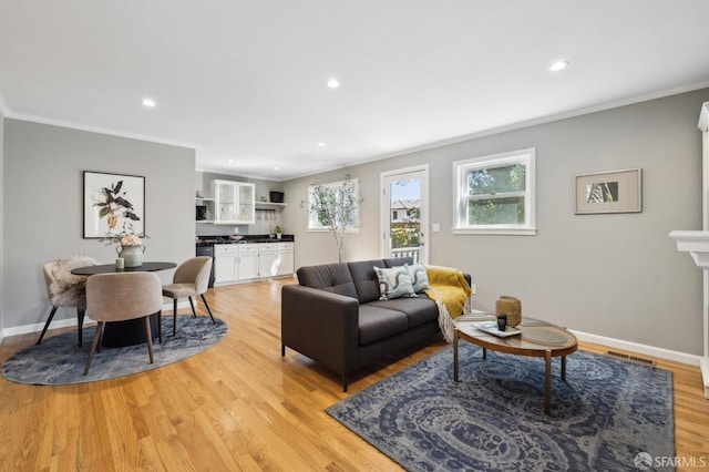 living room featuring visible vents, baseboards, light wood-style floors, and ornamental molding