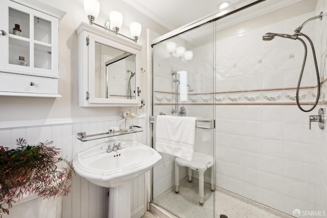 bathroom featuring speckled floor, a wainscoted wall, a sink, a shower stall, and crown molding