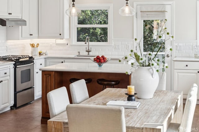 kitchen with a sink, under cabinet range hood, stainless steel gas range oven, white cabinetry, and a kitchen breakfast bar