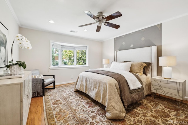 bedroom featuring a ceiling fan, visible vents, wood finished floors, baseboards, and ornamental molding