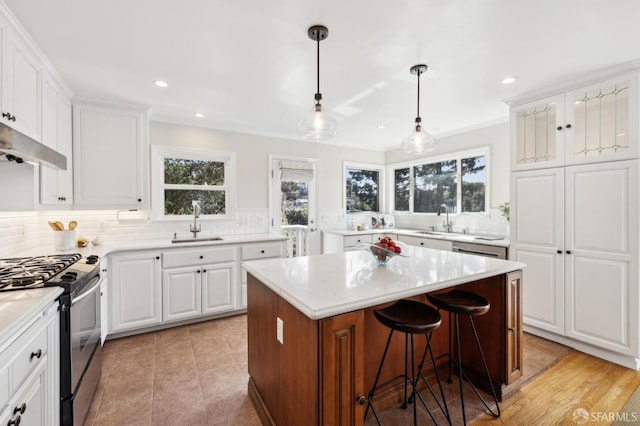 kitchen with gas stove, a sink, light countertops, under cabinet range hood, and tasteful backsplash