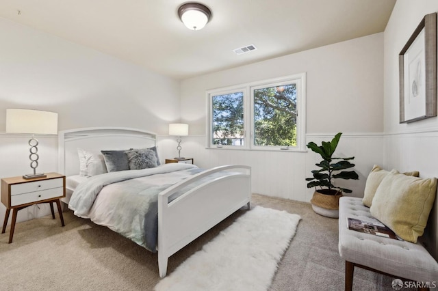 bedroom with light carpet, visible vents, and a wainscoted wall