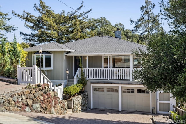 view of front facade with decorative driveway, covered porch, an attached garage, a shingled roof, and a chimney