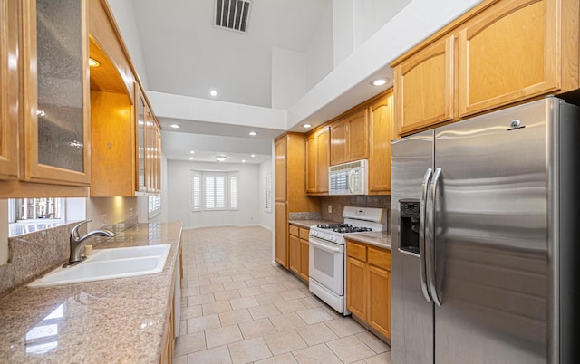 kitchen with tasteful backsplash, a sink, light tile patterned floors, glass insert cabinets, and white appliances