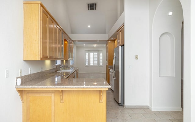 kitchen with a breakfast bar area, a sink, freestanding refrigerator, a peninsula, and recessed lighting
