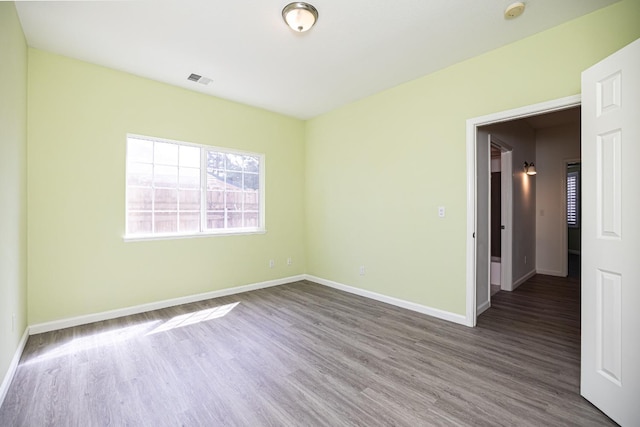 spare room with baseboards, visible vents, and wood finished floors