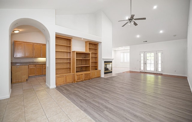 unfurnished living room with baseboards, a ceiling fan, a multi sided fireplace, and high vaulted ceiling