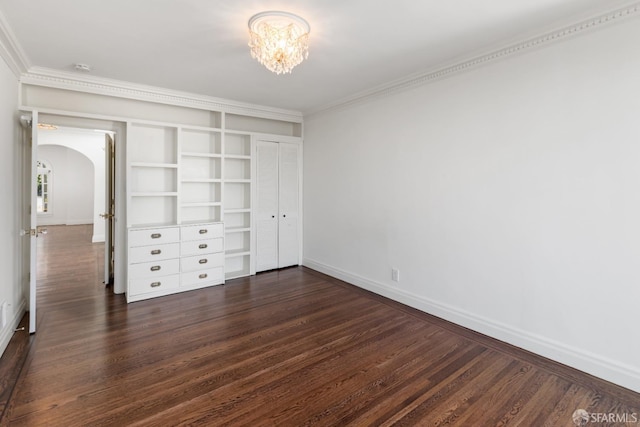 unfurnished bedroom featuring crown molding, baseboards, dark wood finished floors, arched walkways, and a notable chandelier