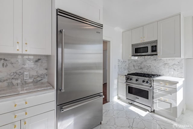 kitchen featuring white cabinetry, decorative backsplash, light stone counters, and premium appliances