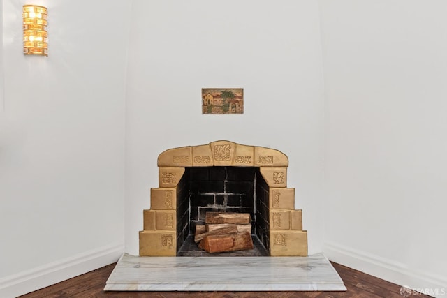 room details featuring baseboards, a fireplace with raised hearth, and wood finished floors