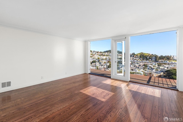 spare room featuring visible vents, a wall of windows, baseboards, and wood finished floors