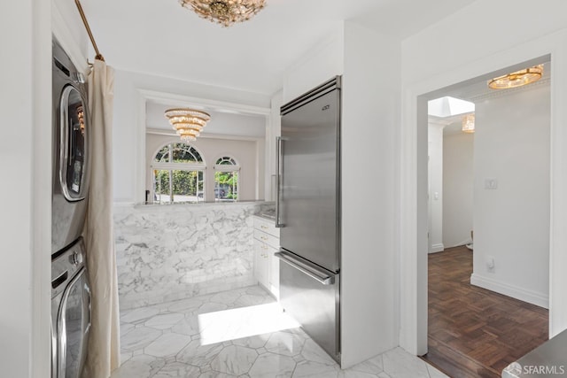 interior space featuring white cabinetry, stacked washer and clothes dryer, built in refrigerator, and a chandelier