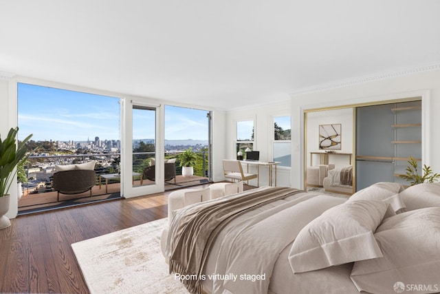 bedroom with a closet, ornamental molding, expansive windows, and wood finished floors