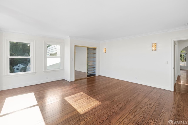 spare room featuring arched walkways, ornamental molding, baseboards, and wood finished floors