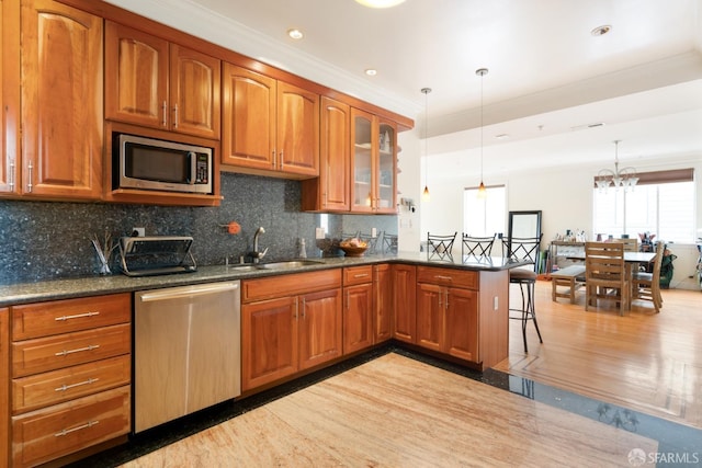 kitchen with appliances with stainless steel finishes, sink, dark stone countertops, hanging light fixtures, and kitchen peninsula