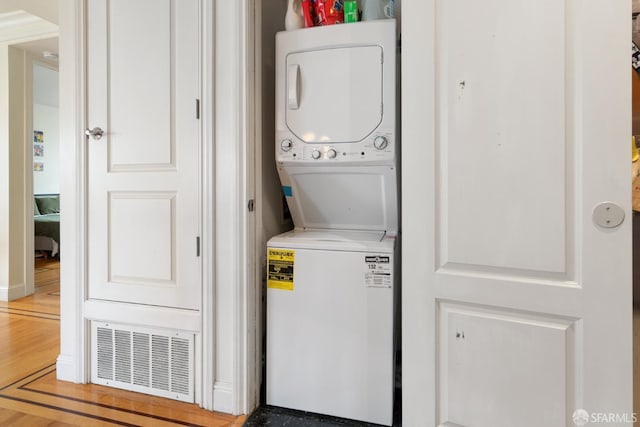 laundry area with hardwood / wood-style flooring and stacked washer / drying machine