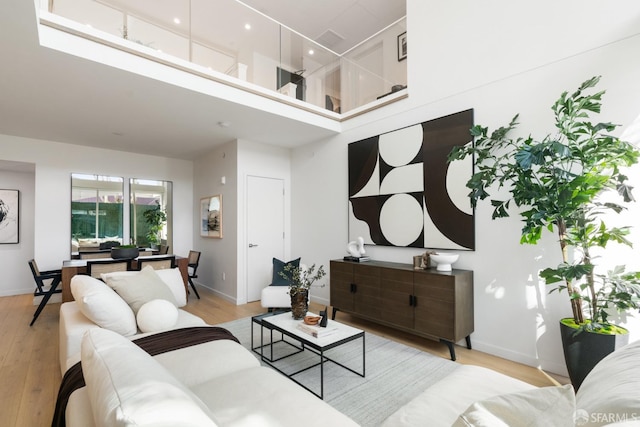 living area with baseboards, a high ceiling, and light wood-style floors