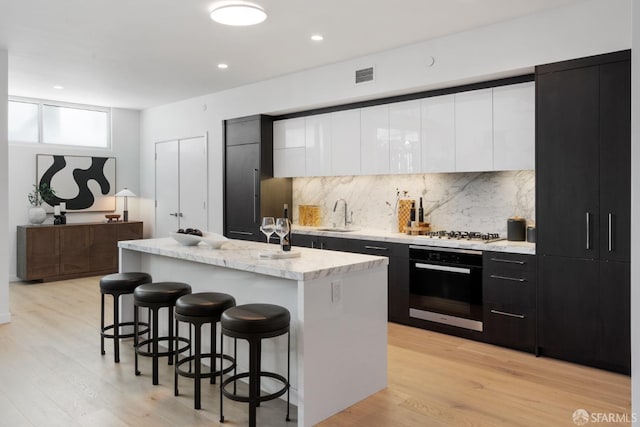 kitchen featuring visible vents, modern cabinets, a breakfast bar, black oven, and dark cabinetry