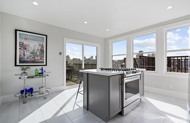 kitchen with gray cabinets, stainless steel gas range oven, light tile patterned flooring, and a kitchen island