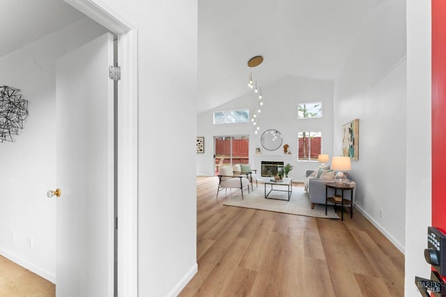 hallway featuring light wood-type flooring, baseboards, and high vaulted ceiling