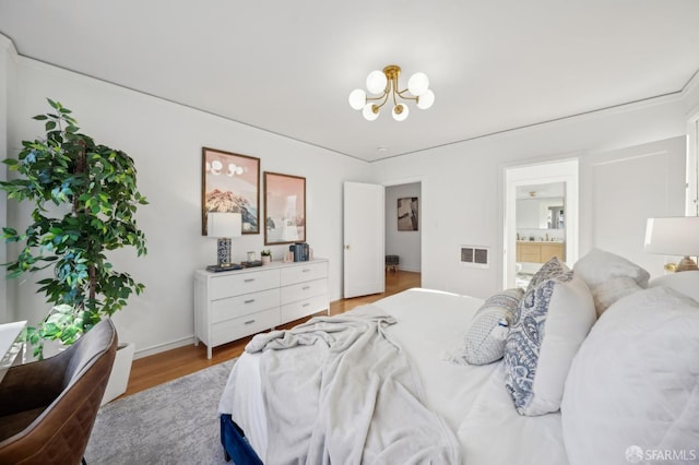 bedroom with an inviting chandelier, ensuite bath, and light hardwood / wood-style flooring