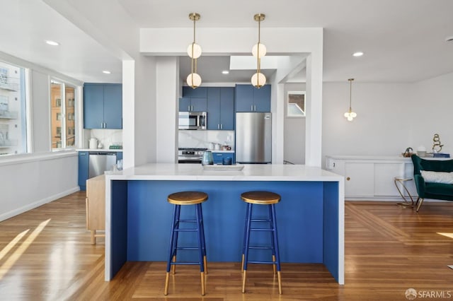 kitchen featuring blue cabinets, dark hardwood / wood-style floors, kitchen peninsula, and appliances with stainless steel finishes