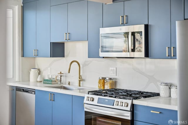 kitchen featuring sink, appliances with stainless steel finishes, tasteful backsplash, light stone countertops, and blue cabinets