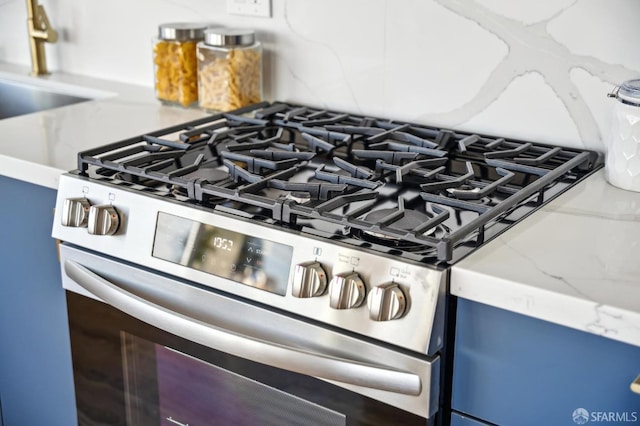 room details with sink, decorative backsplash, stainless steel gas range oven, and light stone countertops