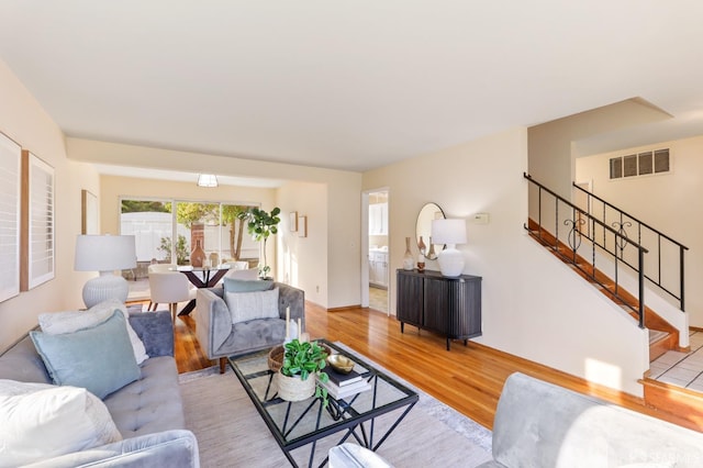living area featuring baseboards, visible vents, light wood finished floors, and stairway