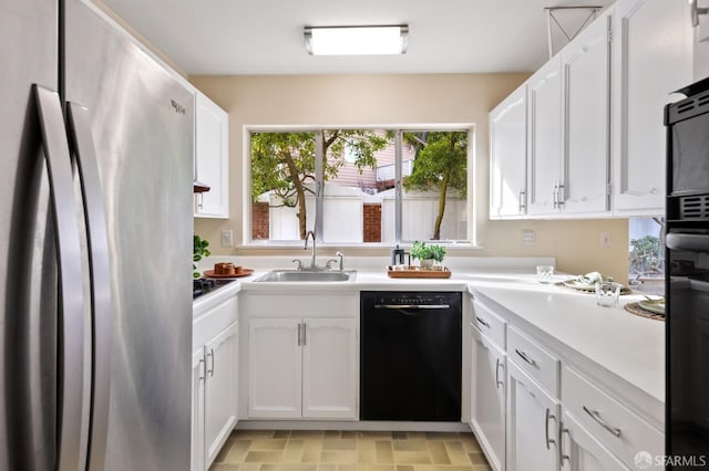 kitchen with a sink, light countertops, freestanding refrigerator, white cabinetry, and black dishwasher