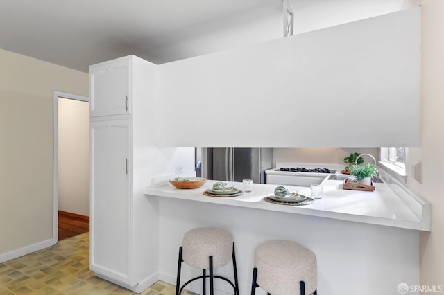 kitchen with white cabinets, a breakfast bar, light countertops, freestanding refrigerator, and baseboards