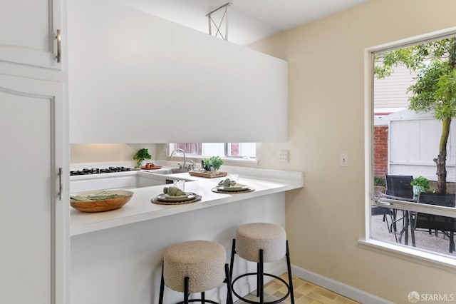 kitchen featuring baseboards, a kitchen breakfast bar, light countertops, a sink, and black gas stovetop