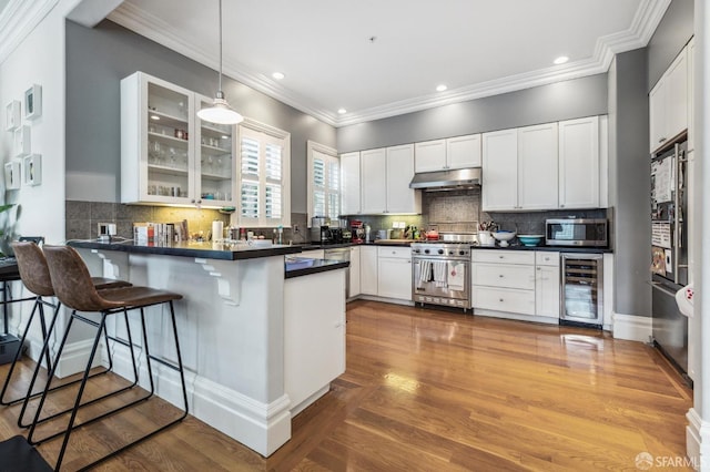 kitchen with appliances with stainless steel finishes, decorative light fixtures, a breakfast bar area, wine cooler, and kitchen peninsula