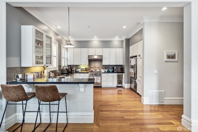 kitchen featuring white cabinetry, decorative light fixtures, appliances with stainless steel finishes, a kitchen breakfast bar, and kitchen peninsula