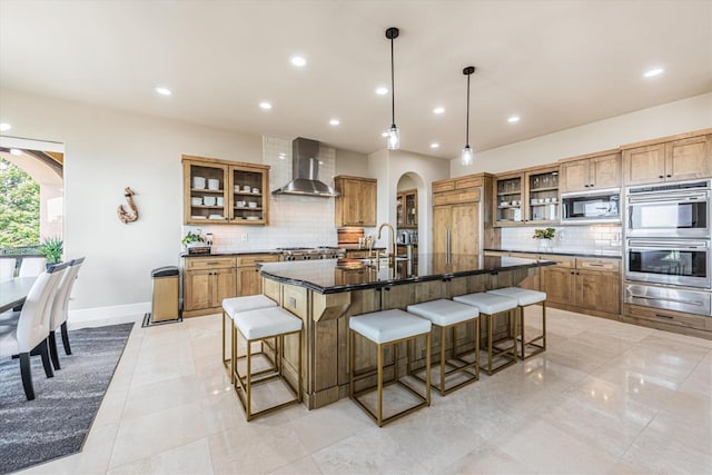 kitchen with a spacious island, pendant lighting, appliances with stainless steel finishes, wall chimney range hood, and tasteful backsplash