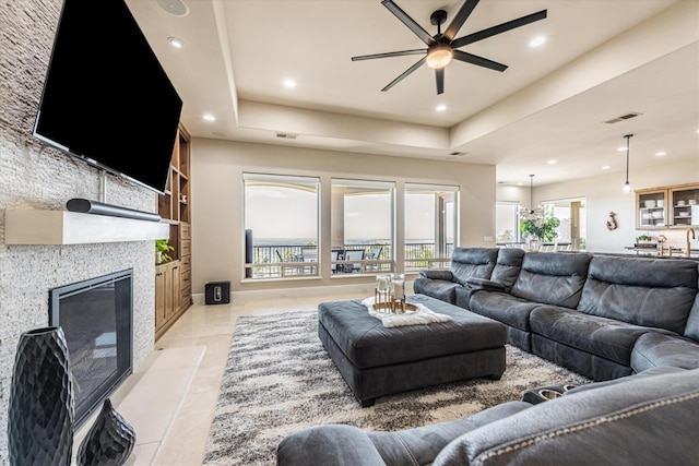 tiled living room with ceiling fan, a tile fireplace, and a tray ceiling