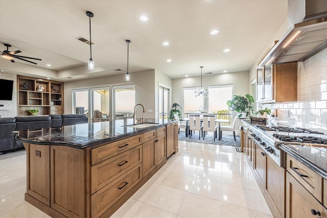 kitchen featuring a spacious island, sink, hanging light fixtures, stainless steel gas cooktop, and dark stone counters