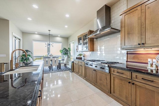 kitchen with decorative light fixtures, stainless steel gas cooktop, dark stone counters, wall chimney range hood, and sink