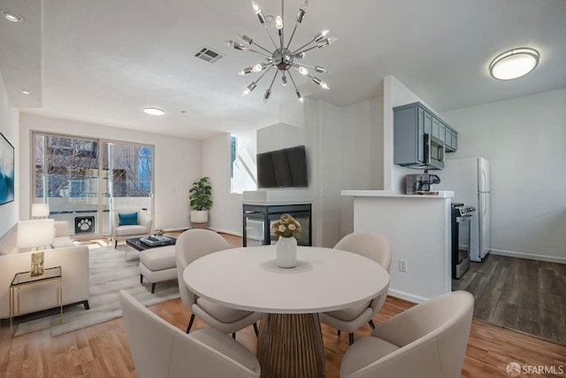 dining area featuring visible vents, a notable chandelier, a multi sided fireplace, and light wood-type flooring