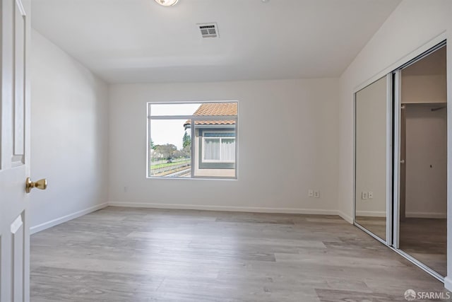 unfurnished bedroom with a closet, baseboards, light wood-style flooring, and visible vents