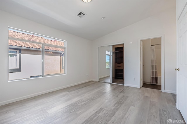 unfurnished bedroom featuring a closet, visible vents, baseboards, lofted ceiling, and light wood-style floors