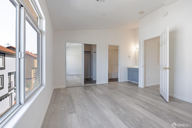 unfurnished bedroom with connected bathroom, baseboards, a closet, and light wood-style flooring