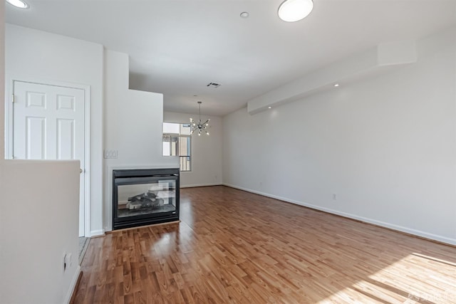 unfurnished living room with a notable chandelier, wood finished floors, a multi sided fireplace, baseboards, and visible vents