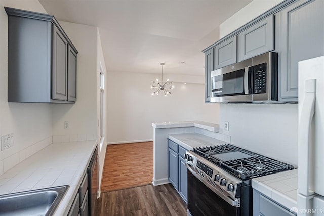 kitchen with tile counters, an inviting chandelier, gray cabinets, stainless steel appliances, and dark wood-style floors