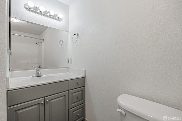 bathroom with a textured wall, toilet, vanity, and walk in shower