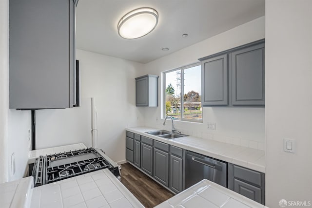kitchen with gray cabinets, a sink, dishwasher, gas range oven, and tile countertops