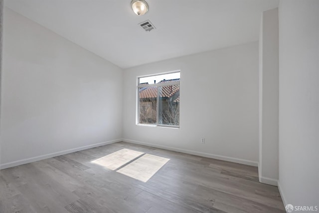 empty room with baseboards, visible vents, wood finished floors, and vaulted ceiling
